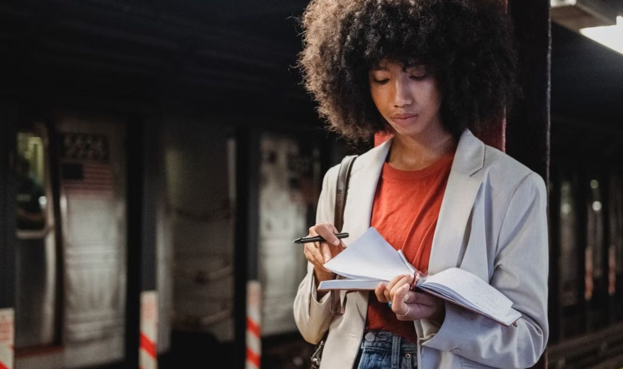 Young woman writing in a notebook at a subway station, capturing urban life and personal reflection
