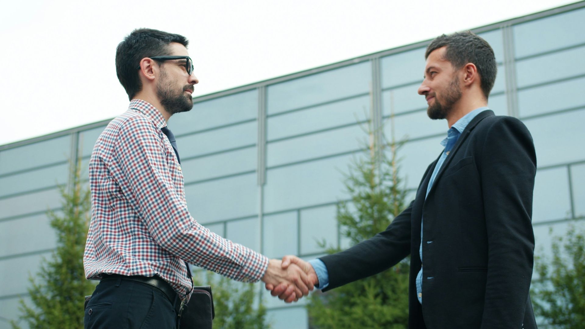 Two businessmen shaking hands outside modern building