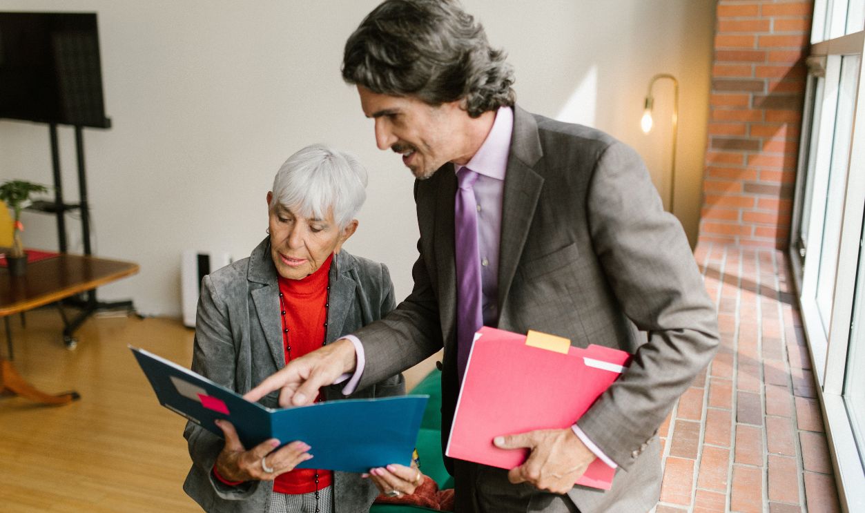 A senior businesswoman and businessman discussing documents in a modern office with natural light.