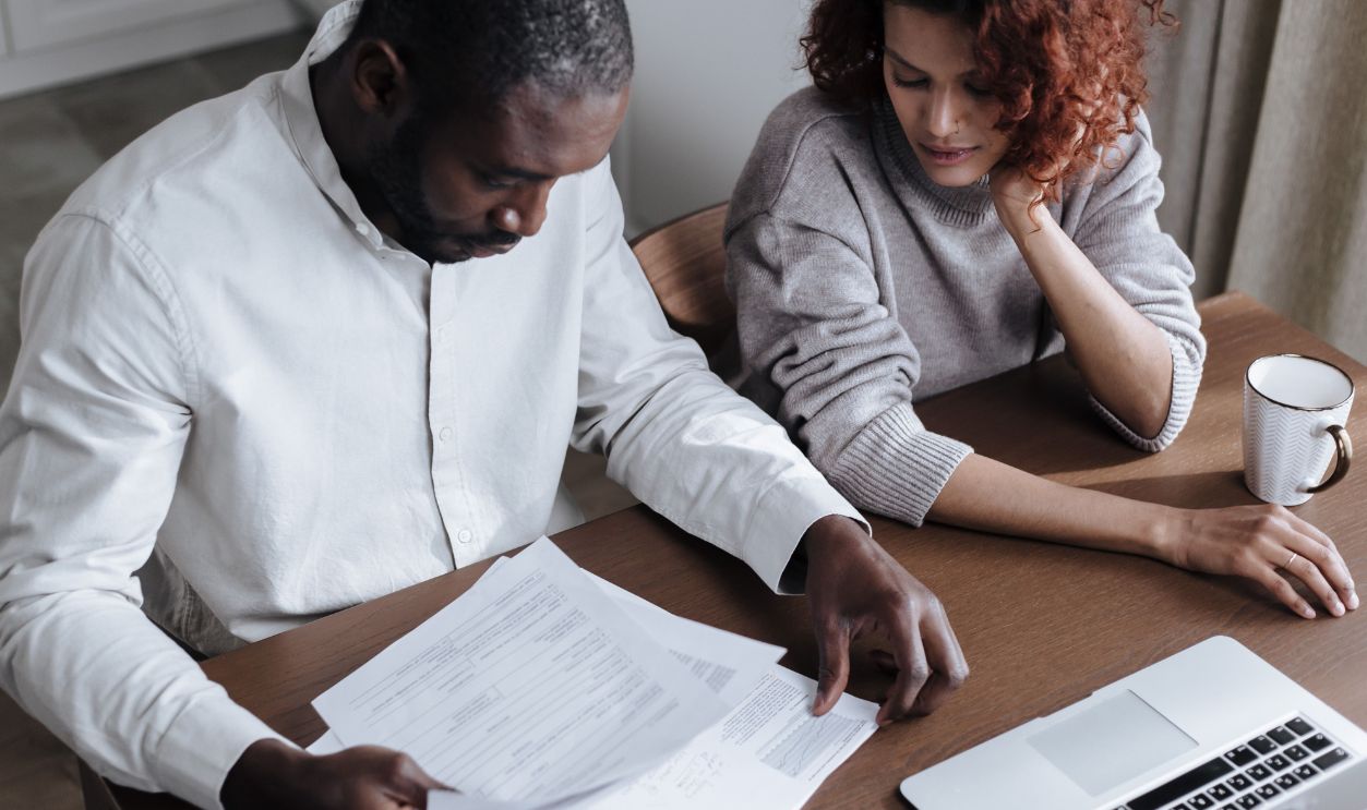 A couple reviews important documents together at a home desk with a laptop.