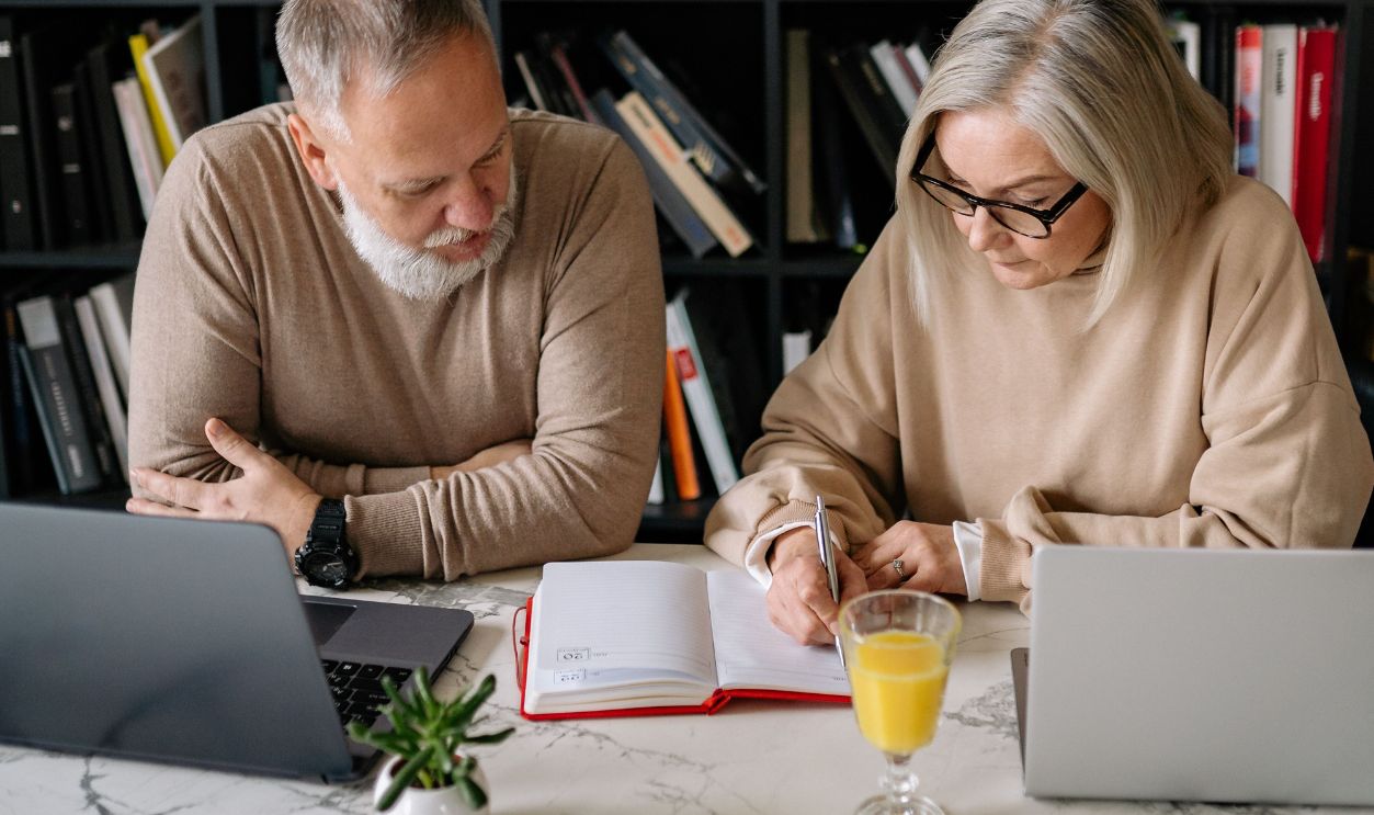Elderly couple working together with laptops and documents in a stylish home study area