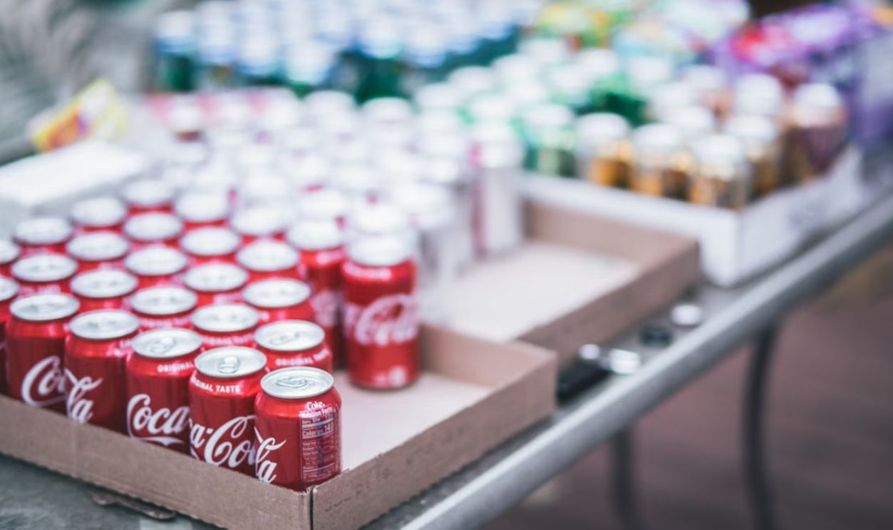 Blurred image of assorted beverage cans on a table, featuring Coca-Cola