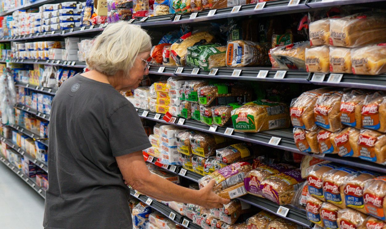 Williston, Vermont, USA - July 21 2026: Elderly shopper examines bags of sliced bread in an aisle in the grocery store