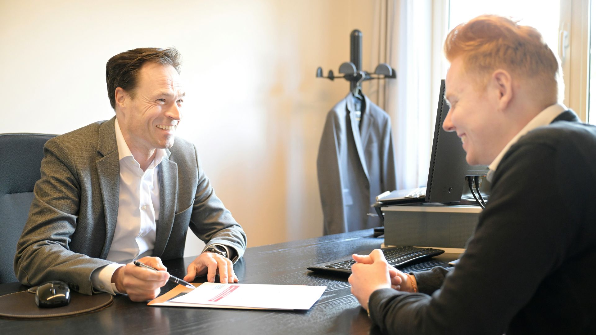 Two smiling men discussing documents at an office desk