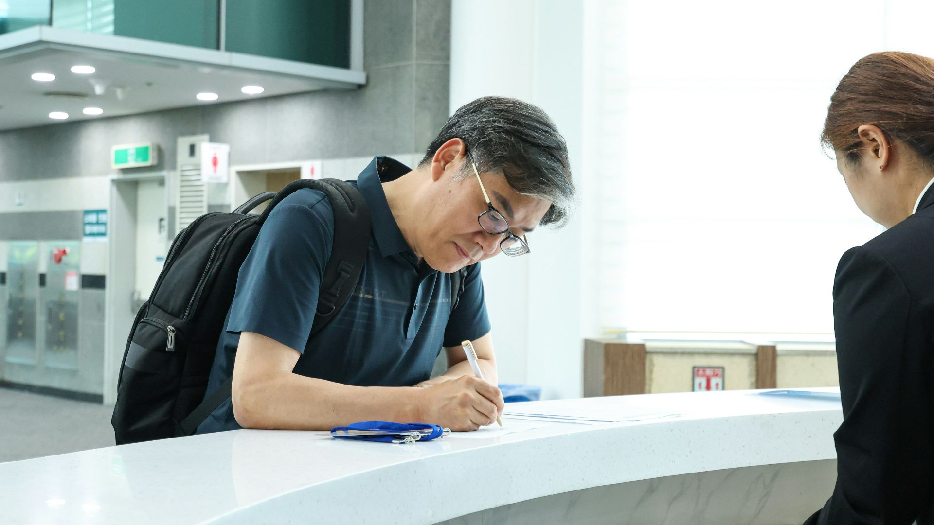 A man signs paperwork at a reception desk