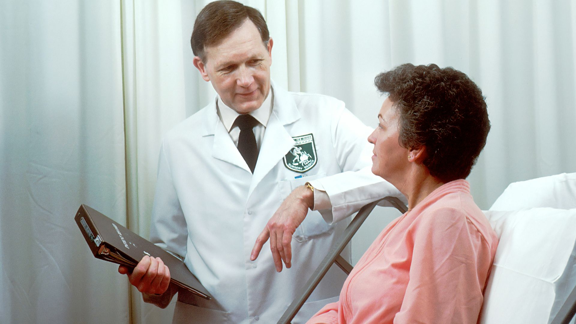 A doctor in a white coat talking to a patient in a hospital bed
