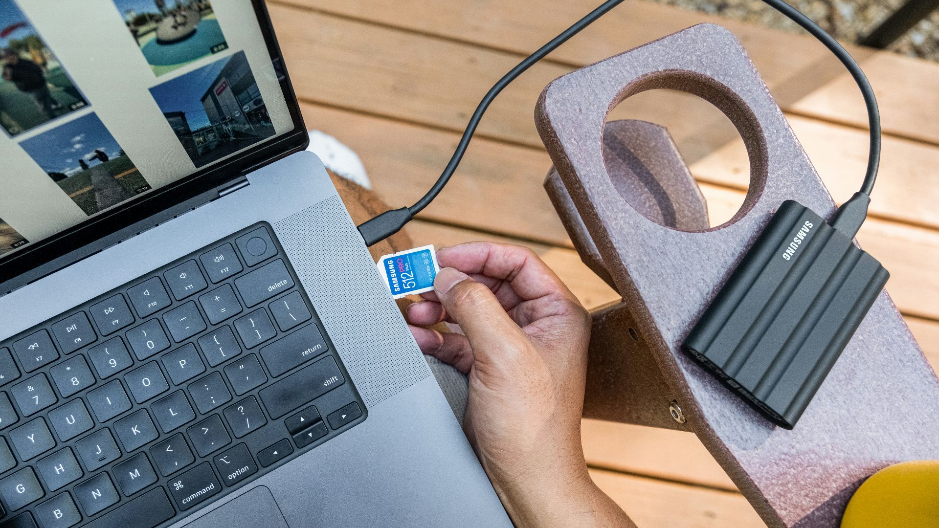 Hand inserting sd card into laptop next to external hard drive