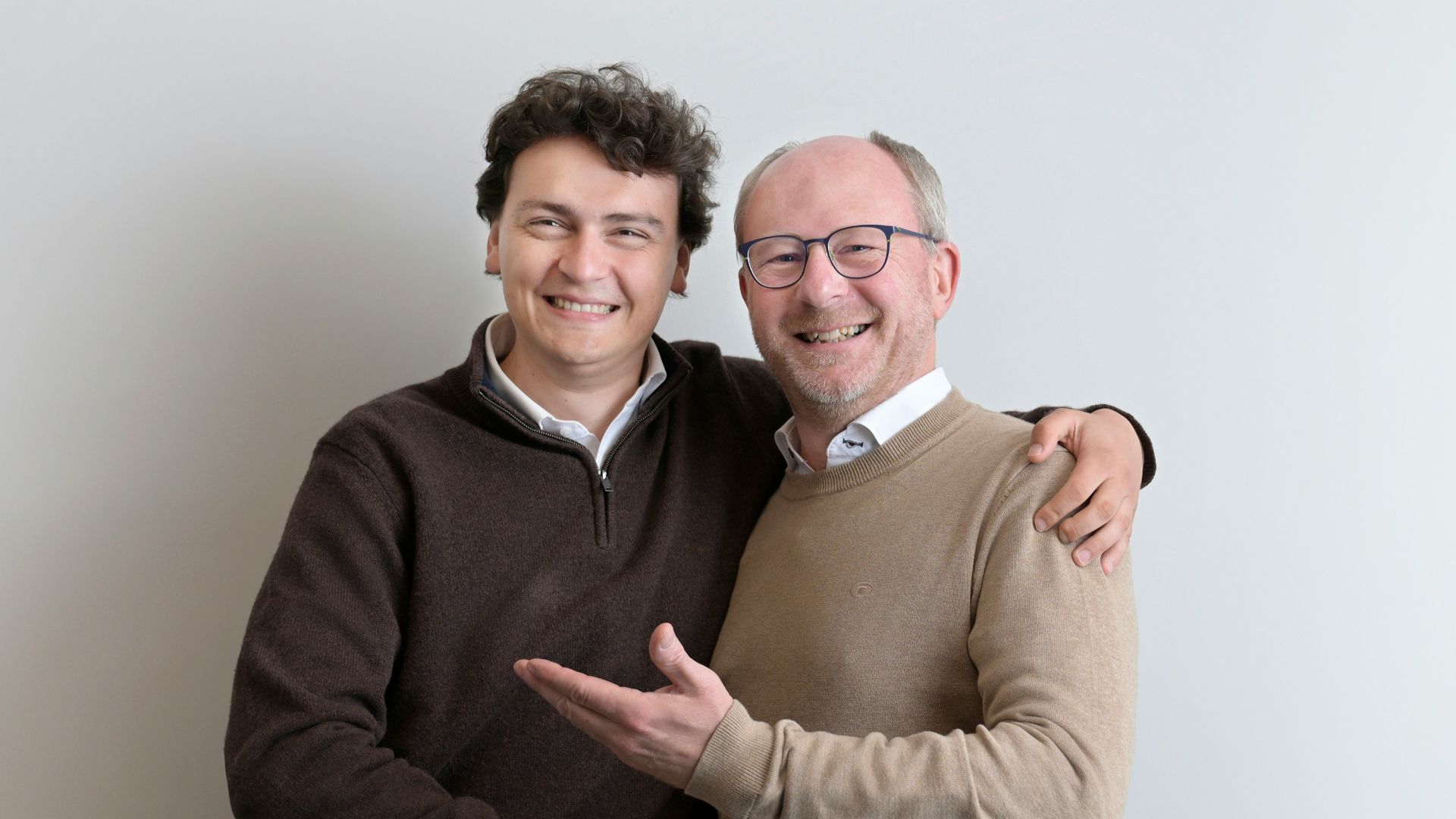 Two smiling men shaking hands against a white wall