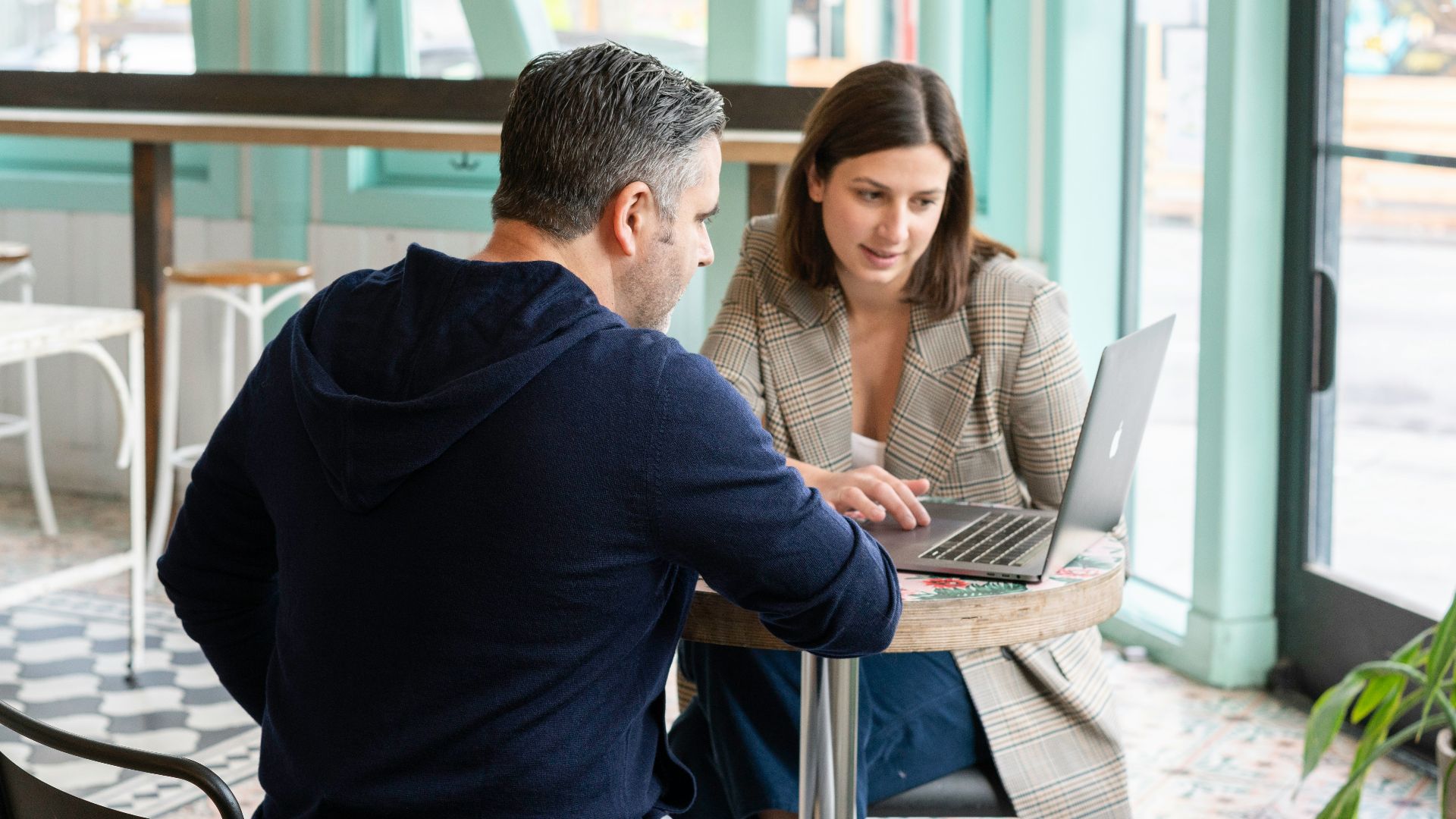 A man and a woman working on a laptop at a cafe table