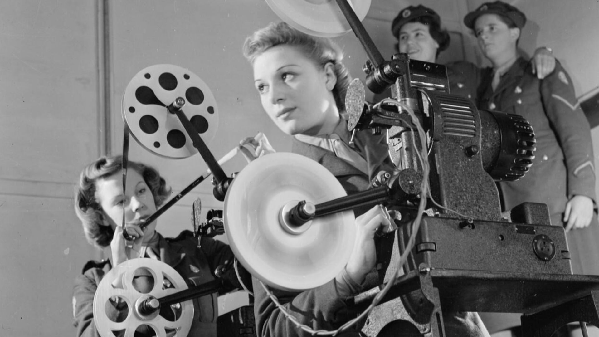 Ats Cine Projector Operators, Aldershot, Hampshire, England, UK, 1941
Two cine projectionists of the Auxiliary Territorial Service operate a 16mm De Vry Simplex Ampro projector at the field stores, Aldershot.  Behind them, two more ATS girls stand in the 