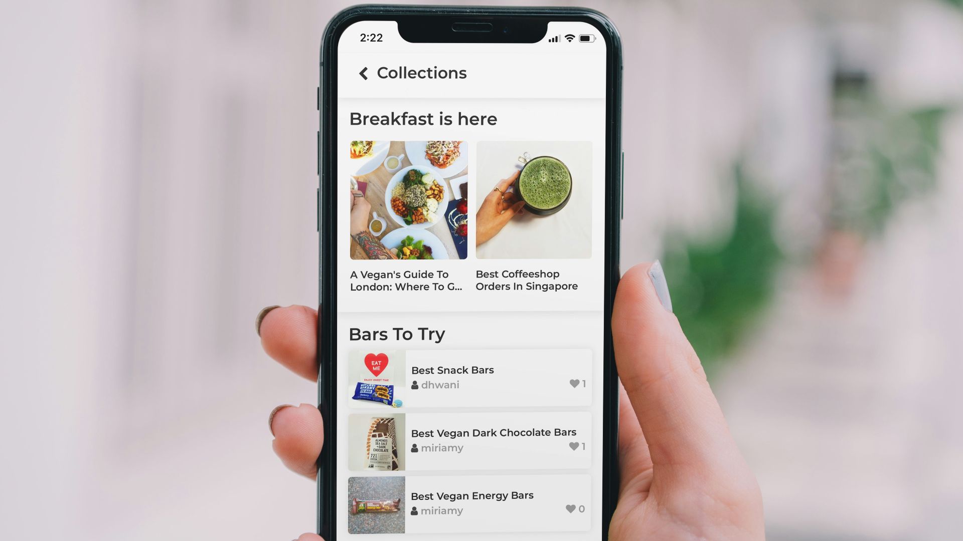 A hand holding a smartphone displaying a food collection app with vegan snack bars