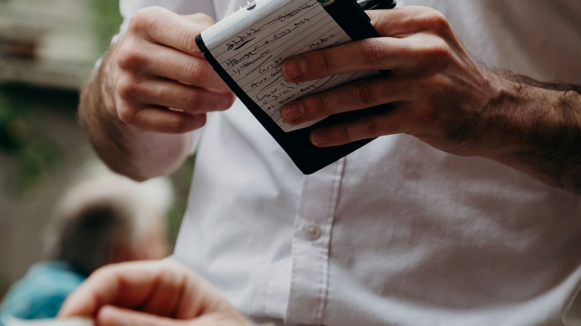 A person in a white shirt holding a notepad and a menu