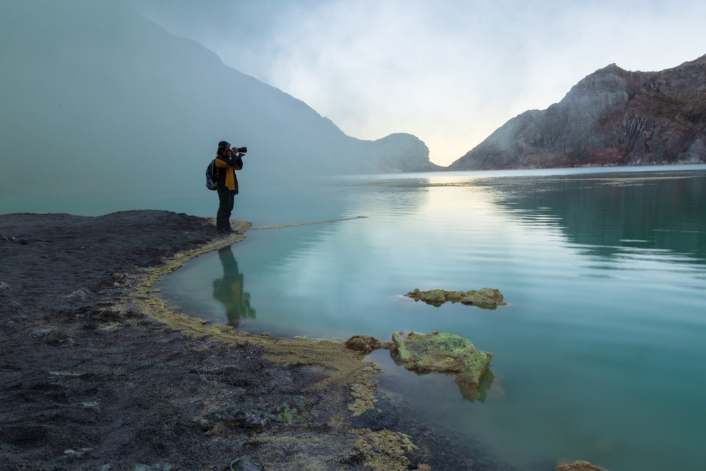 Woman traveler taking pictures at turquoise lake at Kawah Ijen volcano