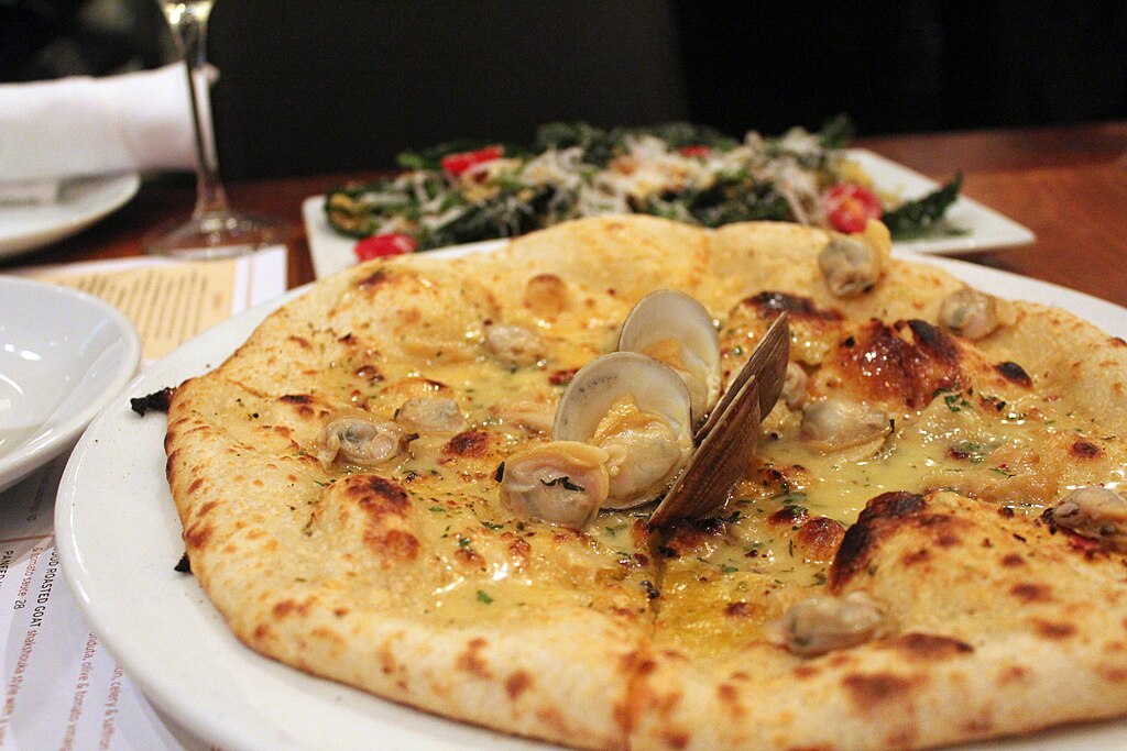 Close-up Photo of a Clam pizza on a white plate placed on a restaurant table