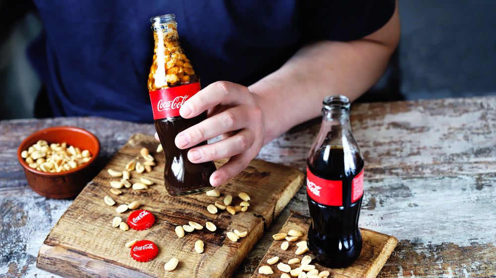 Male hand holds a bottle of Coca Cola with peanuts