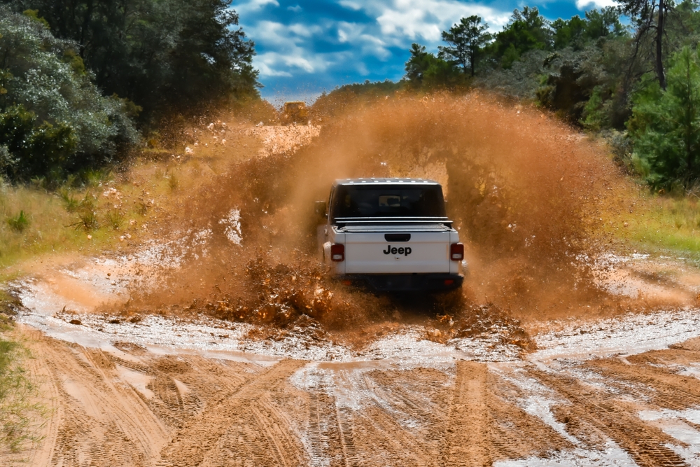 A white Jeep drives through a large mud puddle in the Ocala National Forest during Jeeptoberfest. - 2023