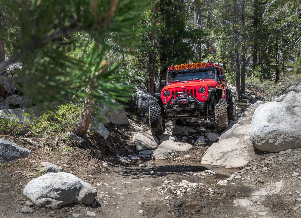 Heavily modified jeep wrangler JK from a distance driving through forest and rocks at Rubicon Trail, Ca. - 2021