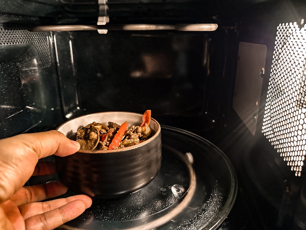 A person is placing a bowl of food into a microwave.