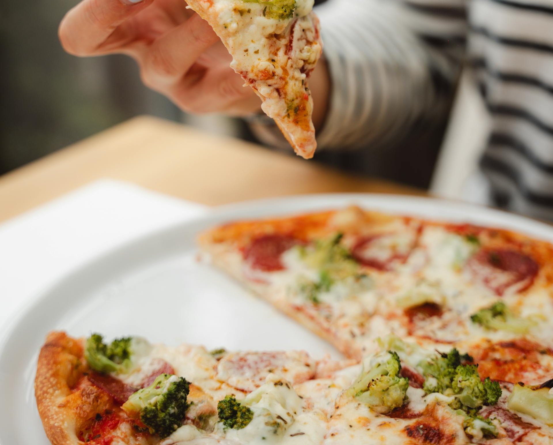 A Person Eating Pizza with Salami and Broccoli