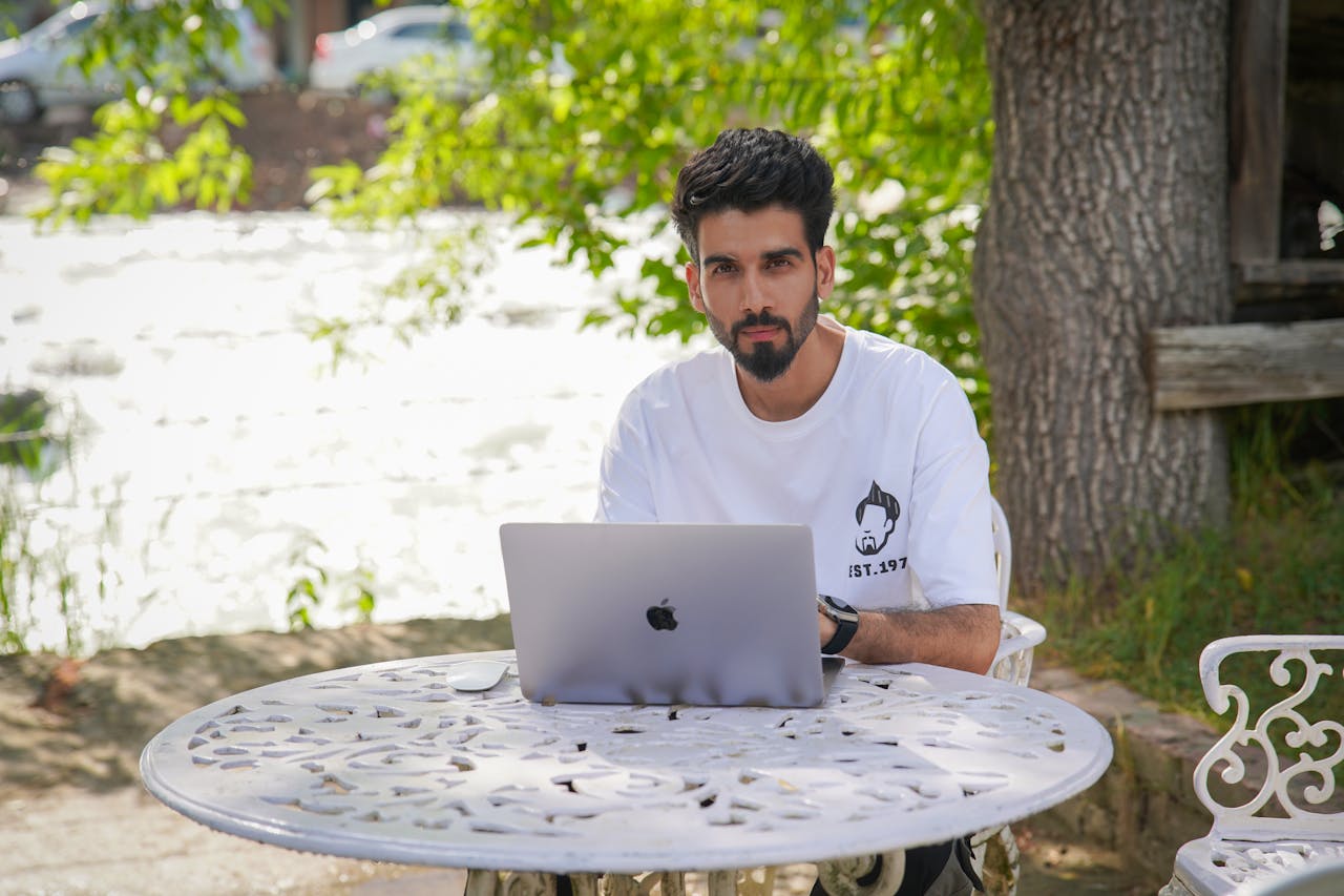 A Man Sitting at a Table in a Garden with a Laptop