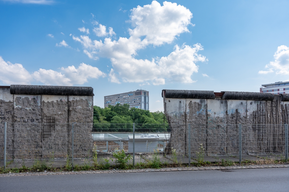 A house is visible in the gap in the old Berlin wall.