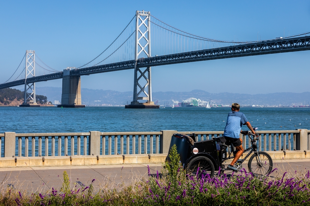 Blue shirt man cycling near Oakland bridge