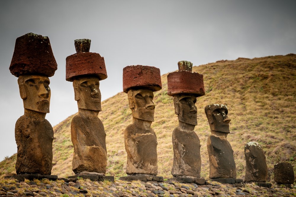 This image features a line of moai statues on Easter Island, each adorned with a red pukao, or hat