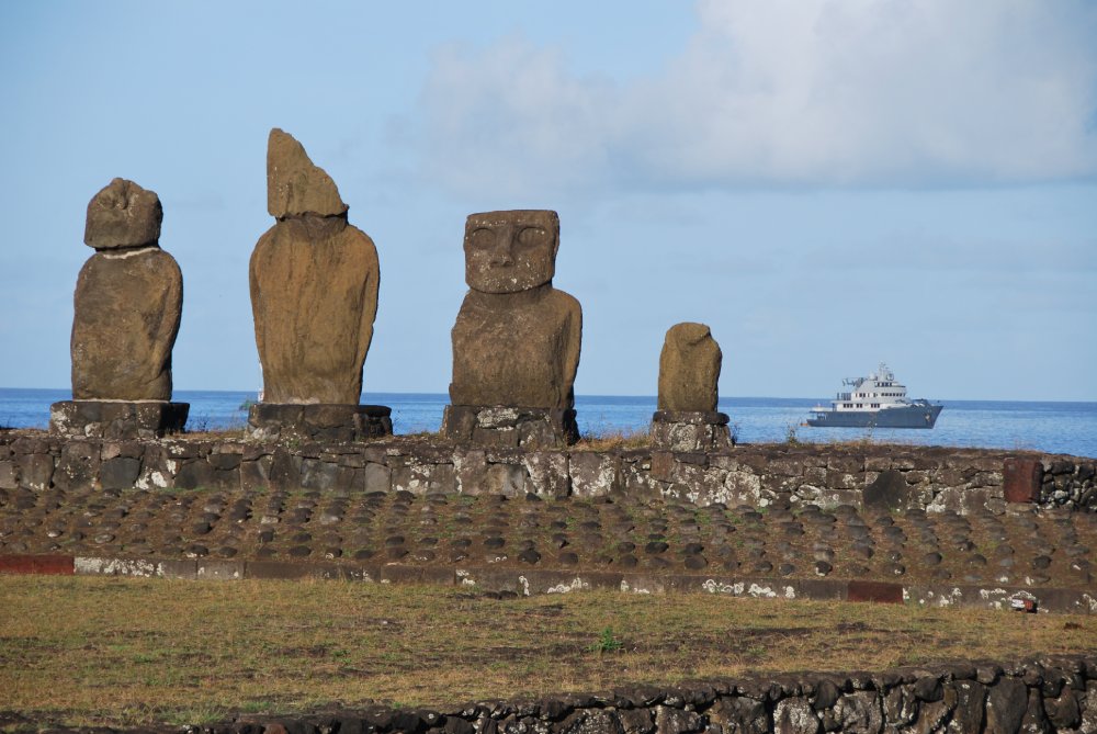 This image features a line of iconic moai statues on Easter Island against a blue sky and ocean