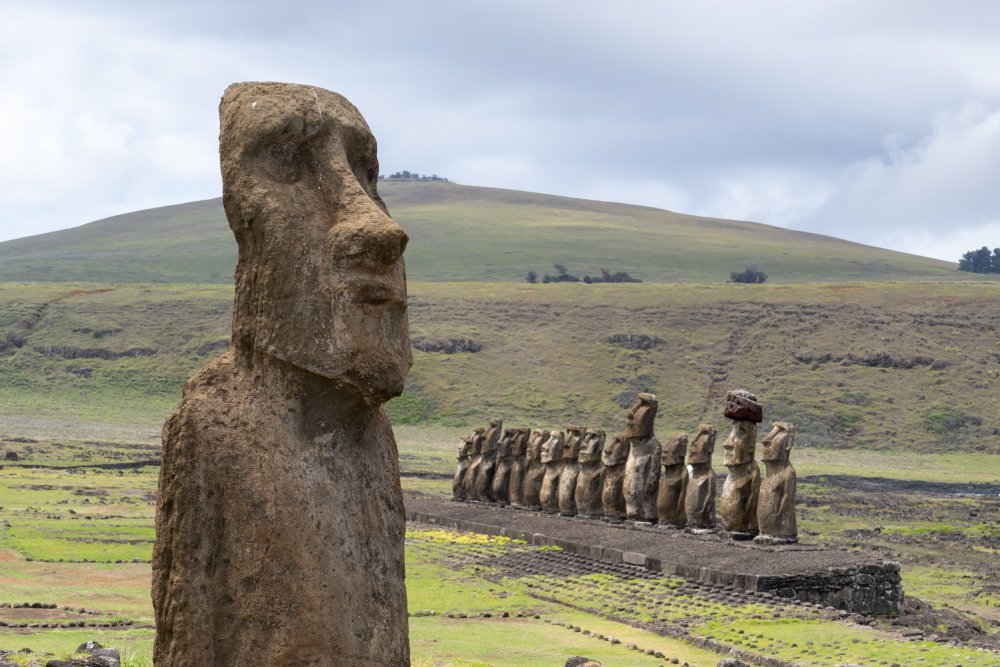 A single moai statue stands in the foreground, other moai statues in the distance.