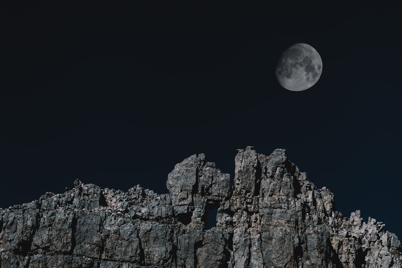 A full moon casts its glow over a jagged cliff face.