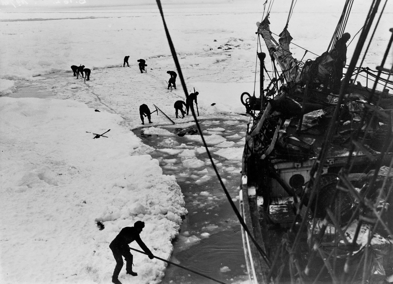 Crew members break up ice with tools to crate an area of open water around the hull of the Endurance to move through - 1915