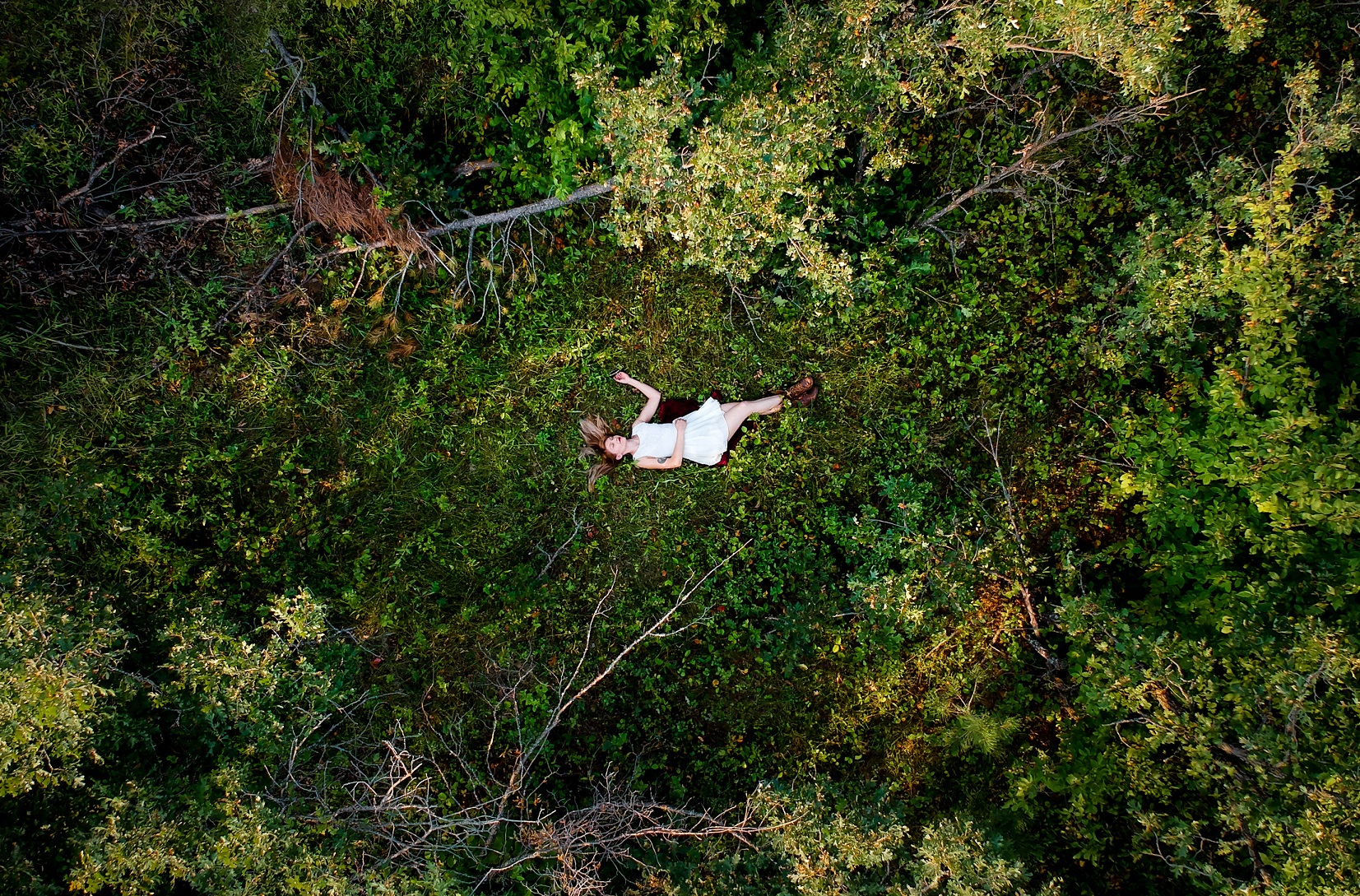 Caucasian Woman laying in forest alone in white dress.