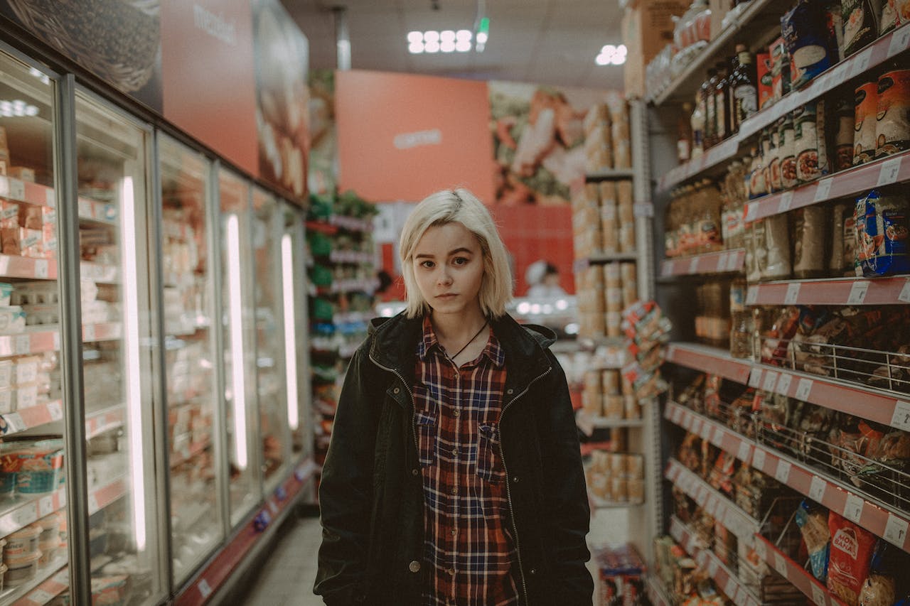 Girl with blonde hair is standing in supermarket .