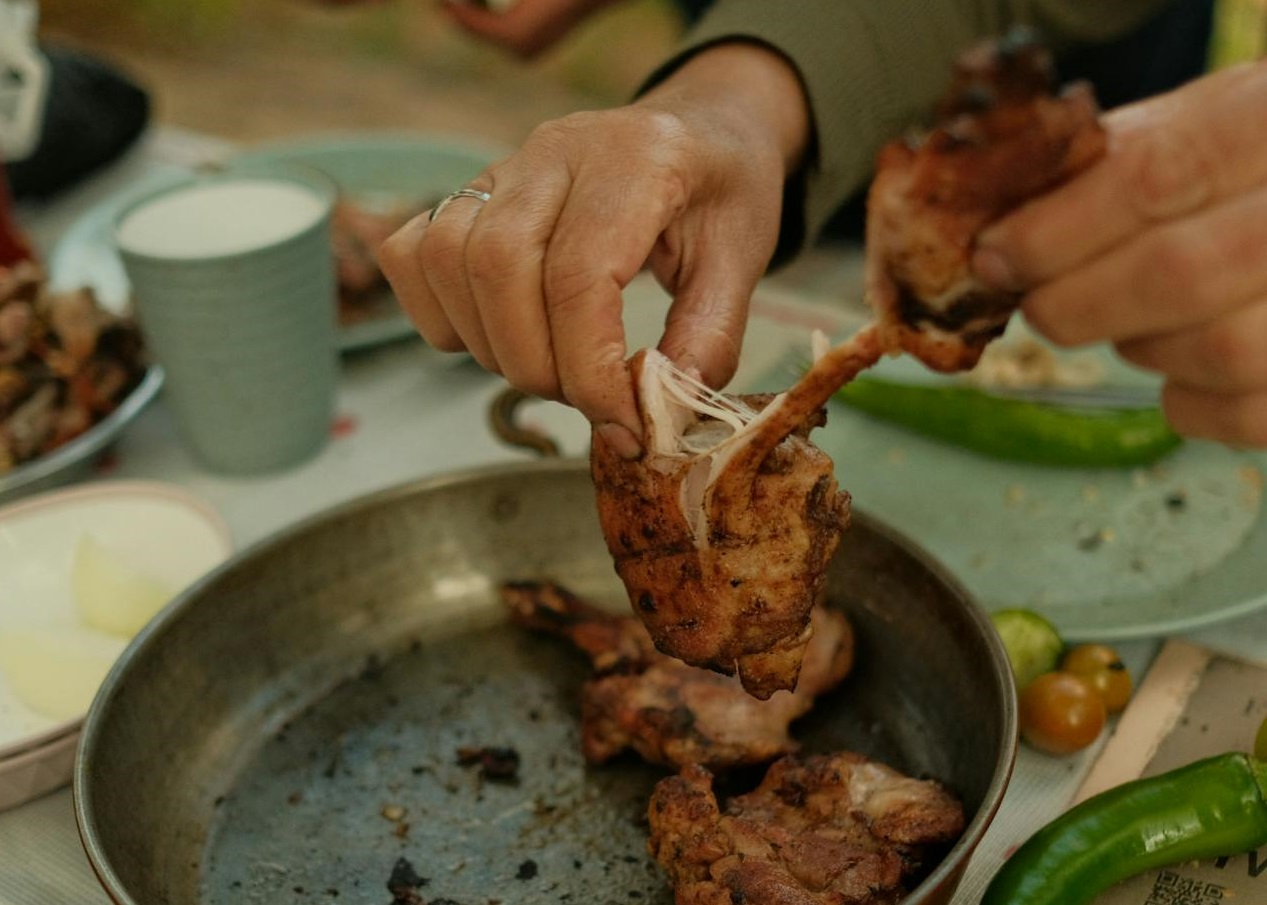 Person taking roasted chicken from a pan.