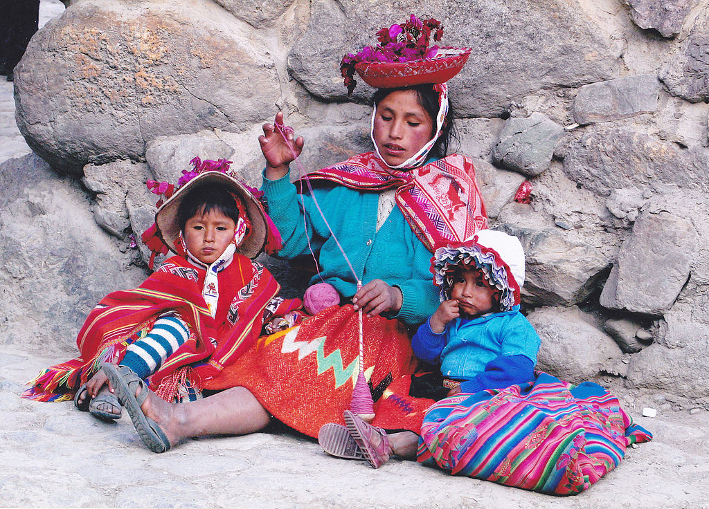Quechua Indian woman spinning with the drop spindle and her two children