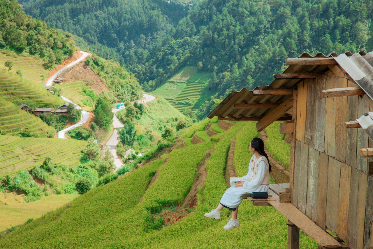 Woman in white dress is sitting over green fields.