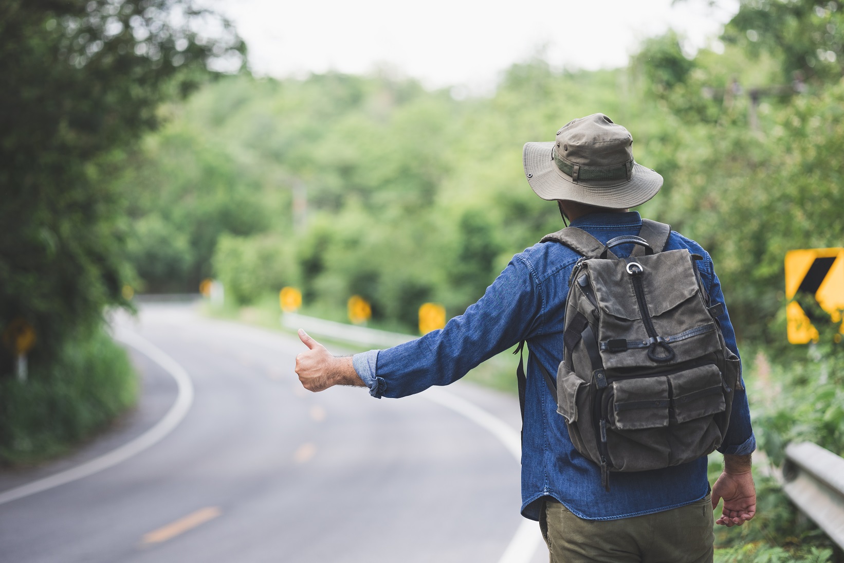 Man hitchhiking on the side of the road.