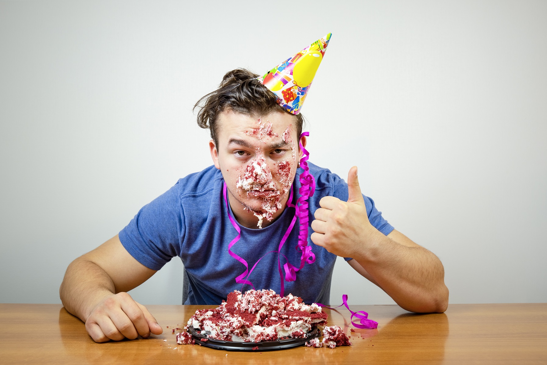 Portrait unhappy good-looking birthday guy with cake on face showing thumb up.