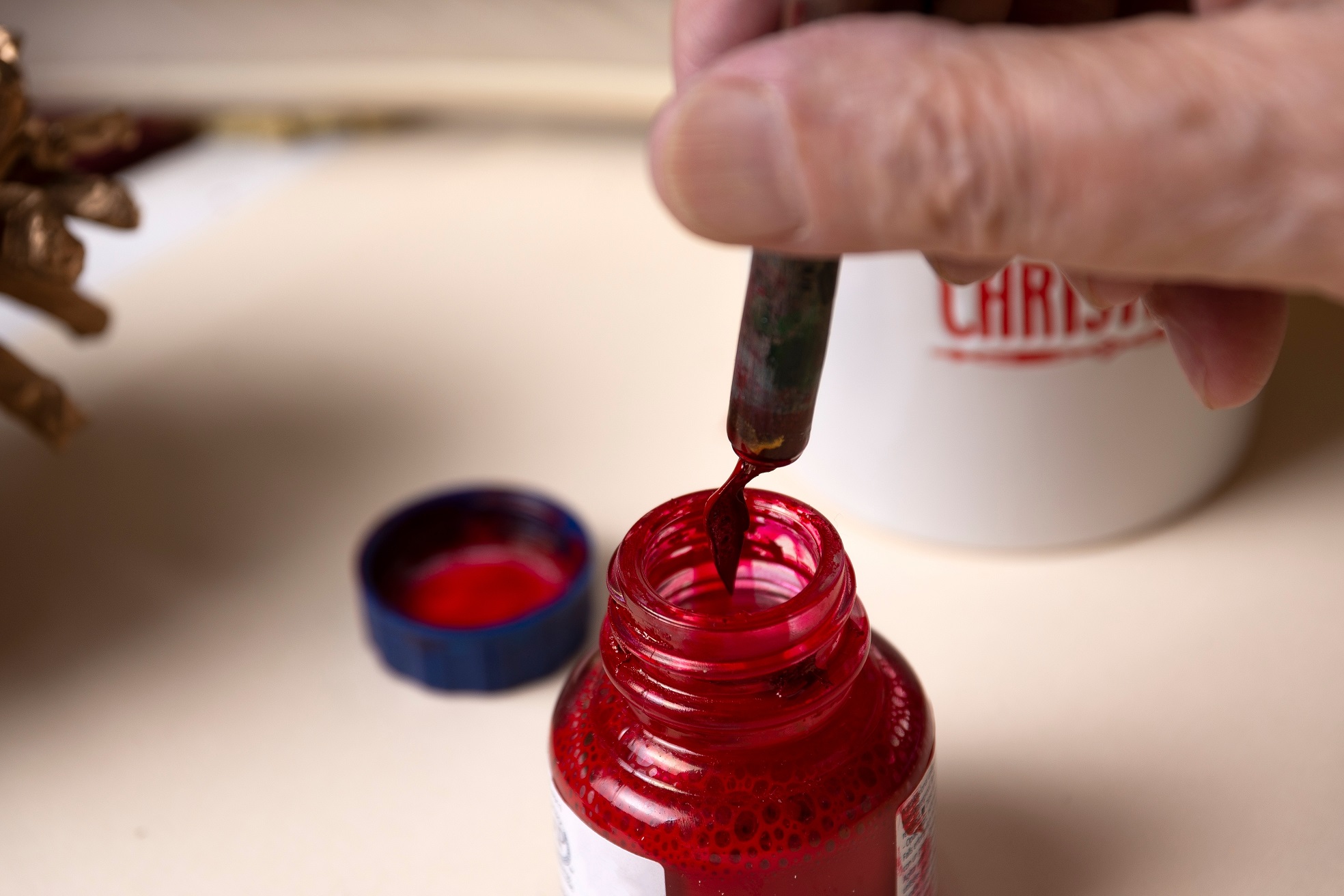 Closeup of an older man's hand loading red ink into a pen from a red ink bottle.