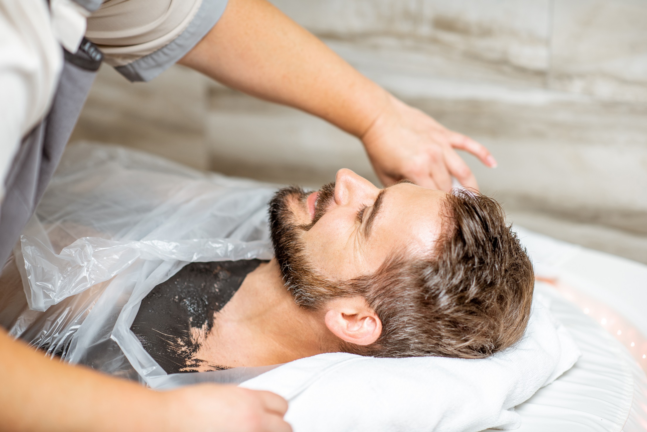 Man during a mud wrapping with special black mud, lying in the spa salon.