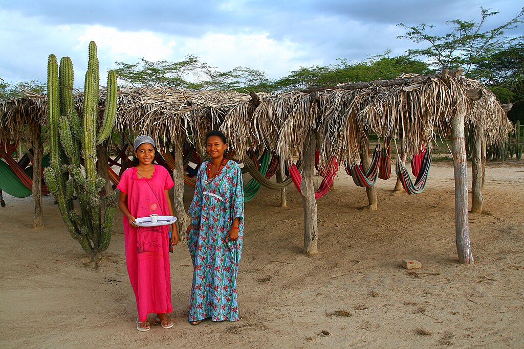 Two Wayuu woman standing next to each other, wearing floral dresses
