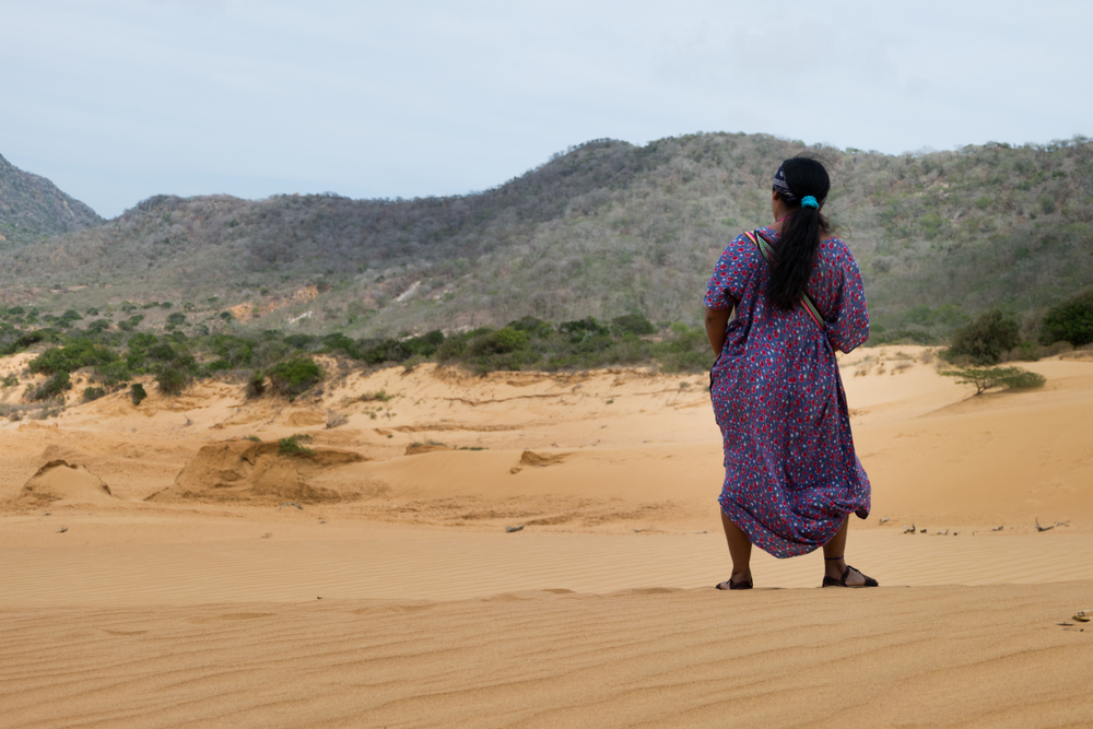 A Wayúu woman back view, in traditional outfit in sand dunes in the desert.