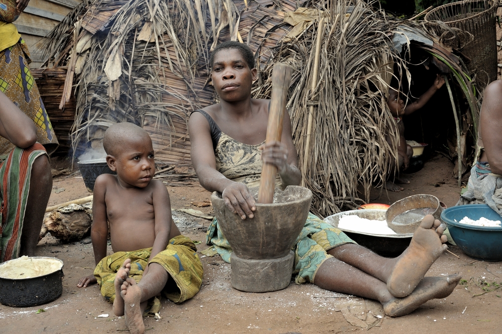 Baka woman cooking food in front of a hut