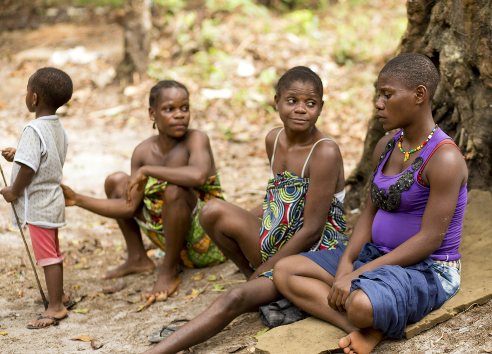 Women from Baka tribe sitting in front of a hut.