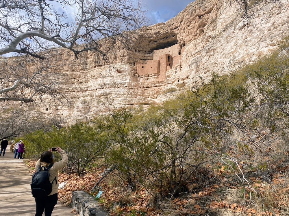A woman taking a photo of Montezuma Castle