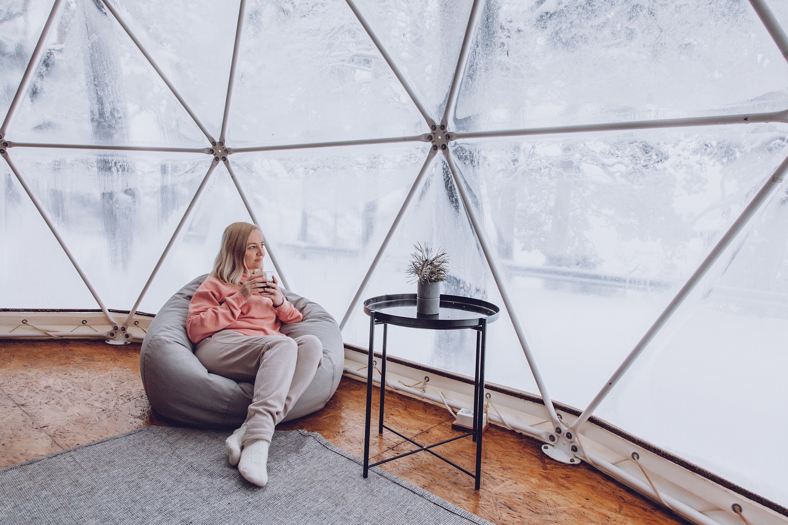A woman is sitting in a geo dome glamping tent in a bag chair