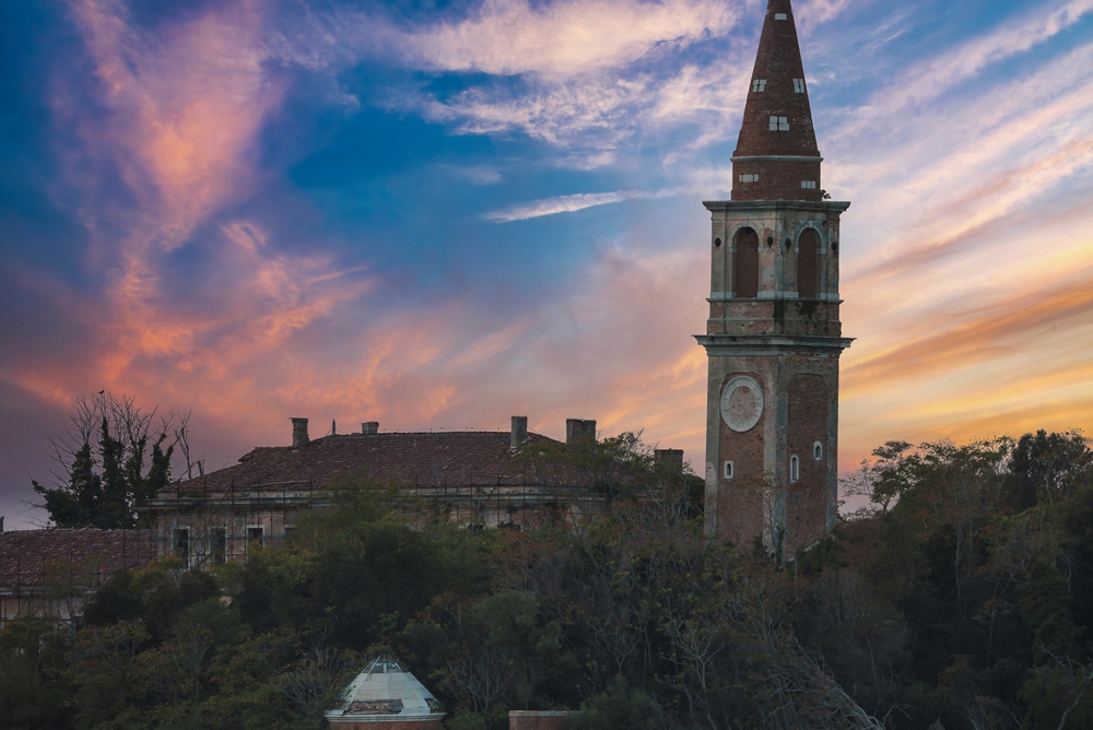 A stunning view of the Poveglia island. A traditional Venetian church with a clock tower overlooking a peaceful body of water at sunset