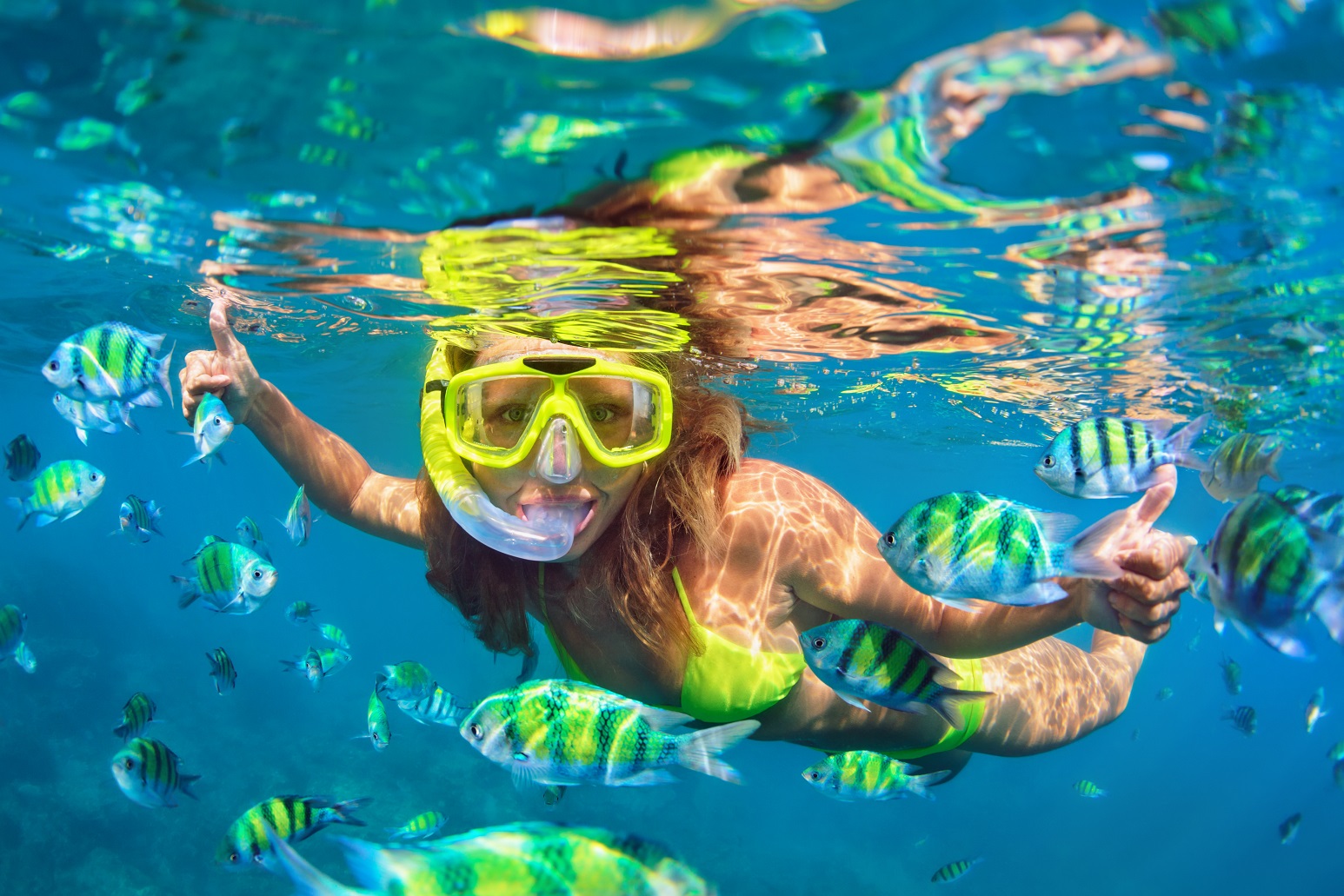 Girl in snorkeling mask dive underwater with fishes.