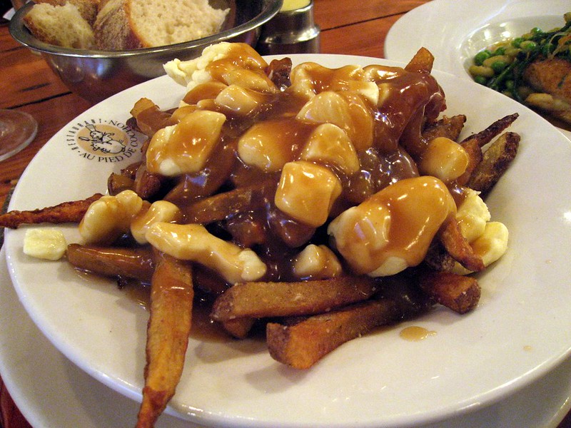 Close-up Photo of Poutine in a white plate placed on a wooden table