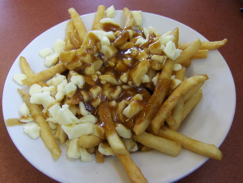 Close-up Photo of Poutine in a white plate placed on a wooden table